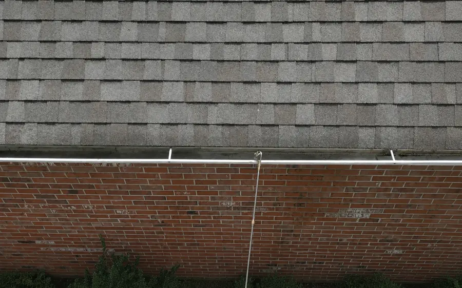 Extension pole clearing a second-story gutter over a fenced yard — gutter guard cleaning Jacksonville